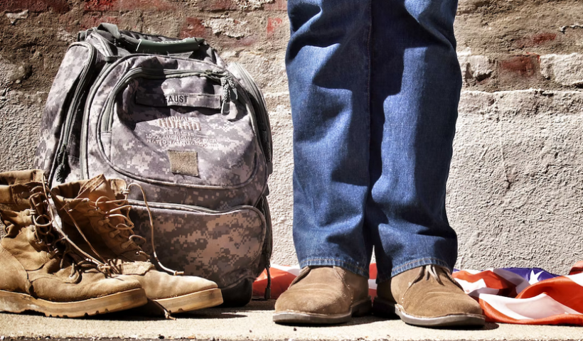 a pair of military boots next to a backpack and a person’s shoes